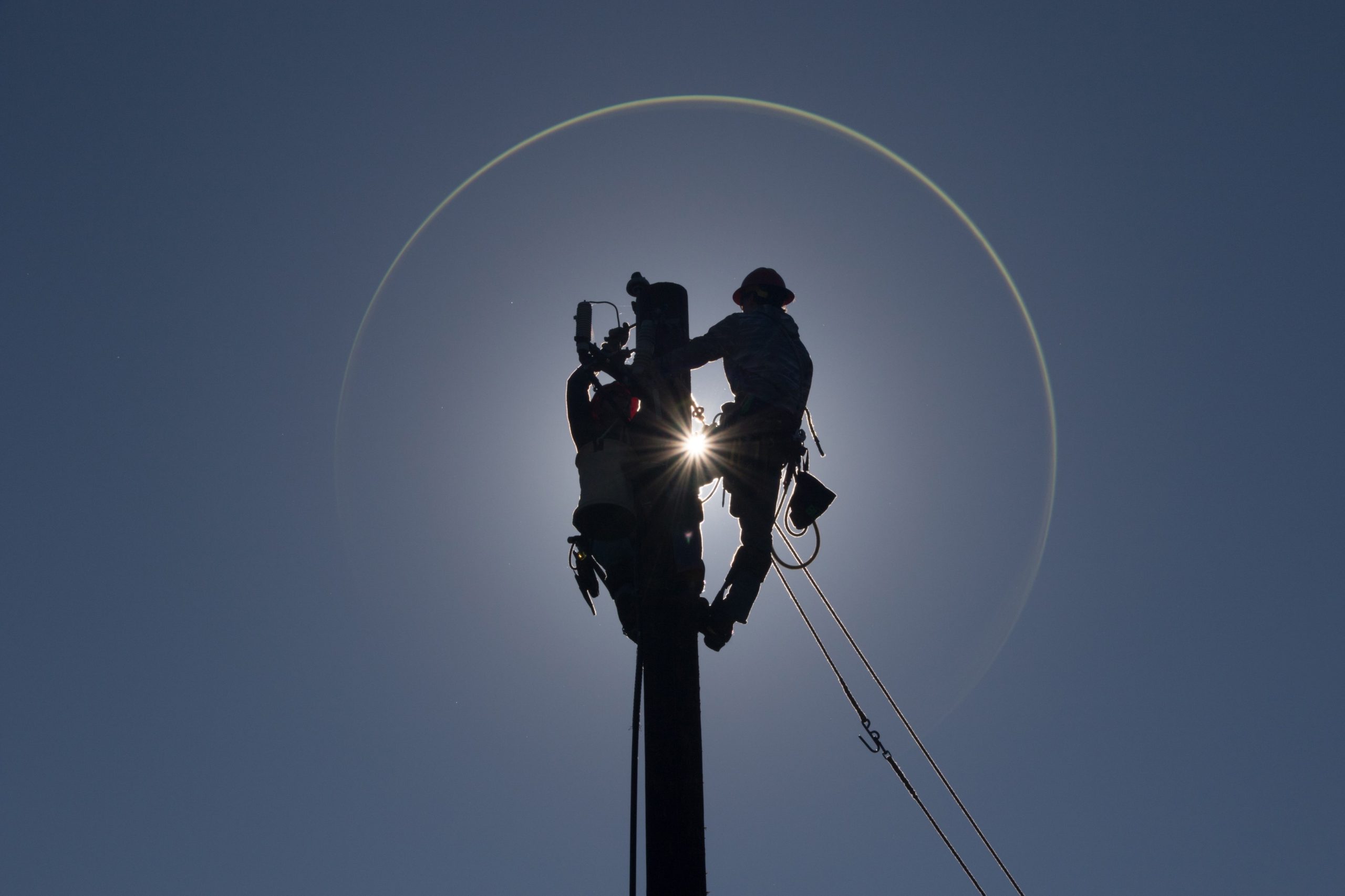 The silhouette of two electrical distribution students working at the top of a pole