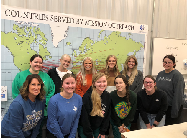 SRA club members and advisor in front of map of countries served by Mission Outreach