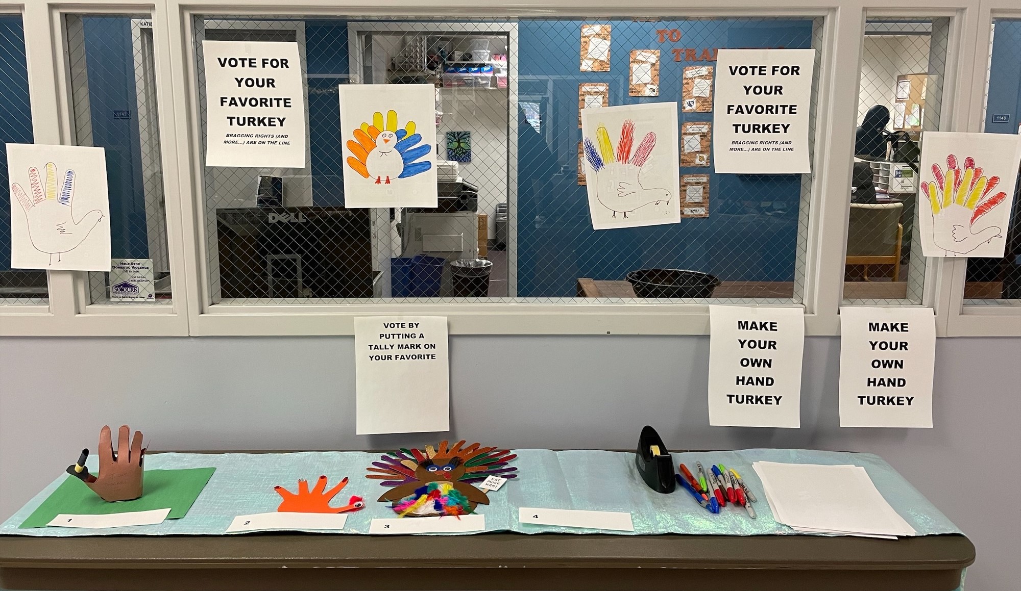 Four hand turkeys to vote on: 1) 3D with pilgrim hat, 2) orange, 3) multi-feathered and multi-colored holding a sign and 4) no turkey. Signs up to make your own hand turkey to decorate the area.