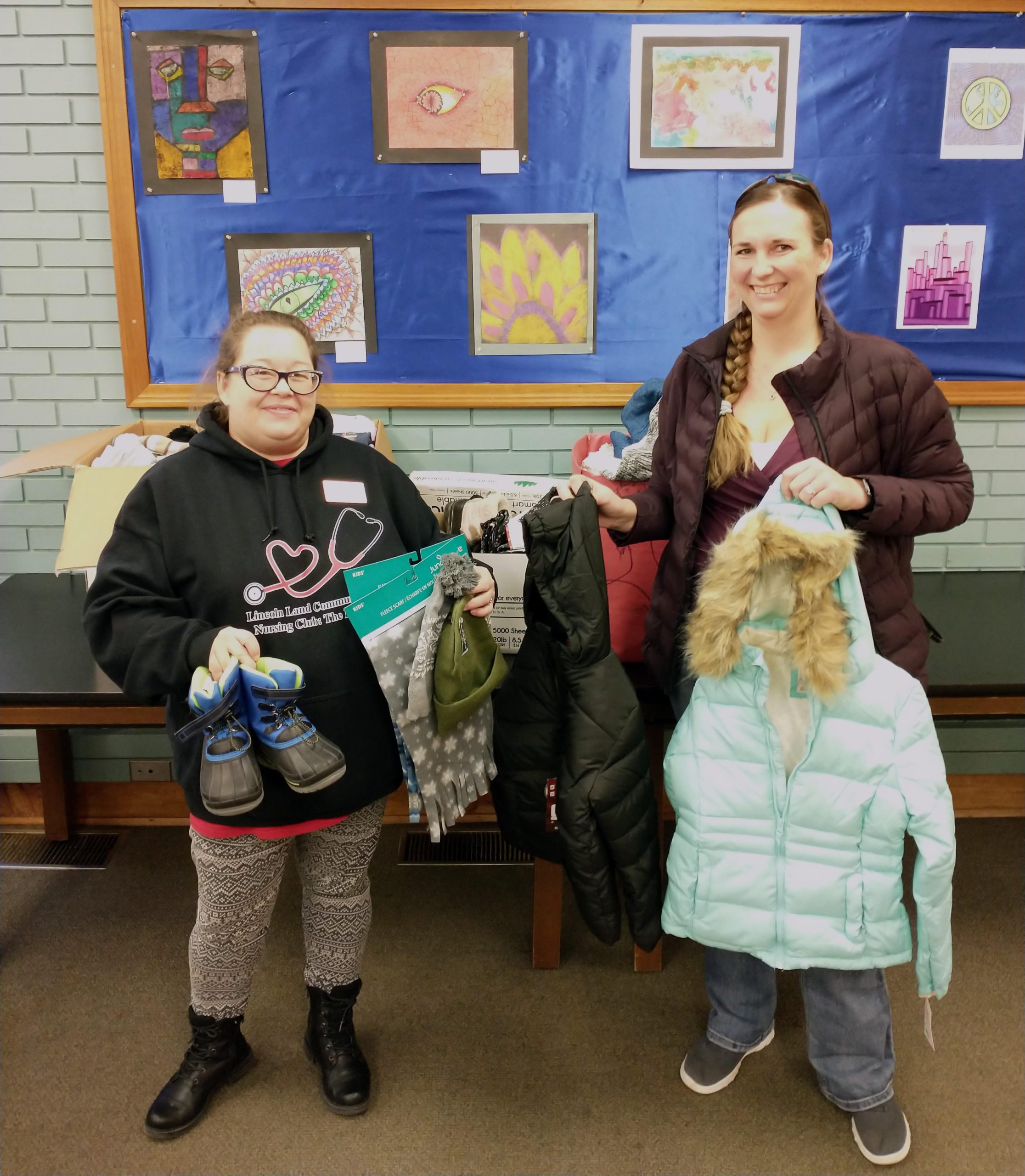 Kim Young and Sarina Sloman holding winter clothing to donate to District 186 schools.
