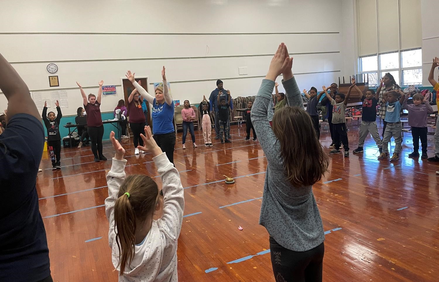 Student with their hands over their heads as they stand in a big circle in the gym