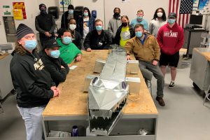 Students in the sheet metal fabrication class stand around a table with a six-foot-long alligator sculpture made of metal ductwork.