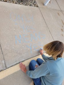 Student chalking a sidewalk with message of "Only yes means yes."