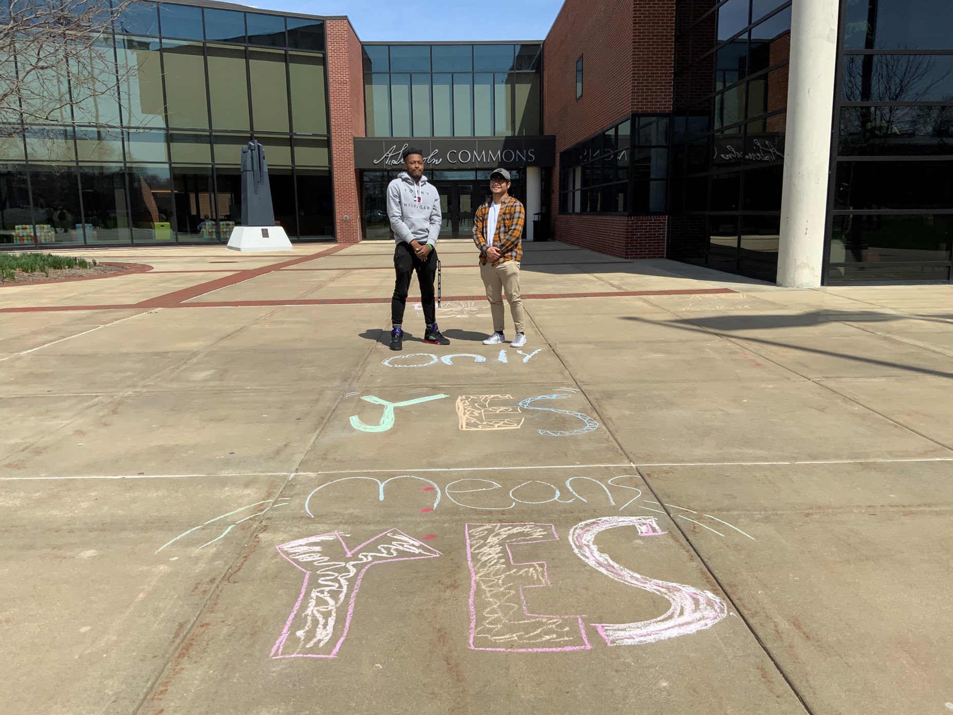 Two male students in front of A. Lincoln Commons. Sidewalk says, "Only yes means yes."