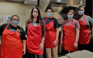 Club advisor with four students in kitchen wearing red aprons