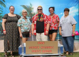 Financial Aid staff standing in front of beach backdrop with their boat, HMS Money Hunnies Party Barge