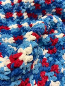 Crocheted blanket with dark blue, light blue, red and white colors.