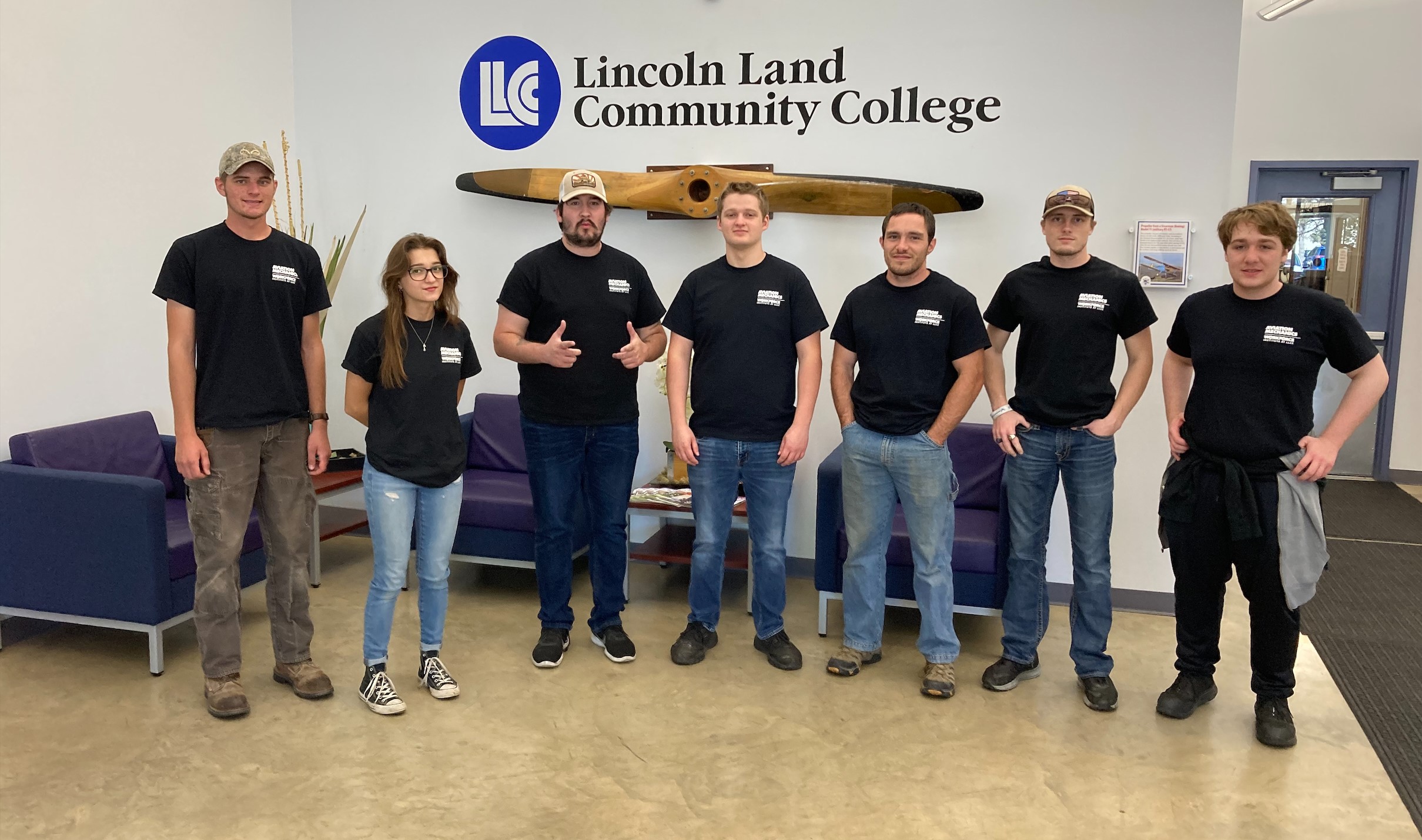 Aviation students in front of the propeller on the wall at LLCC's Aviation Center