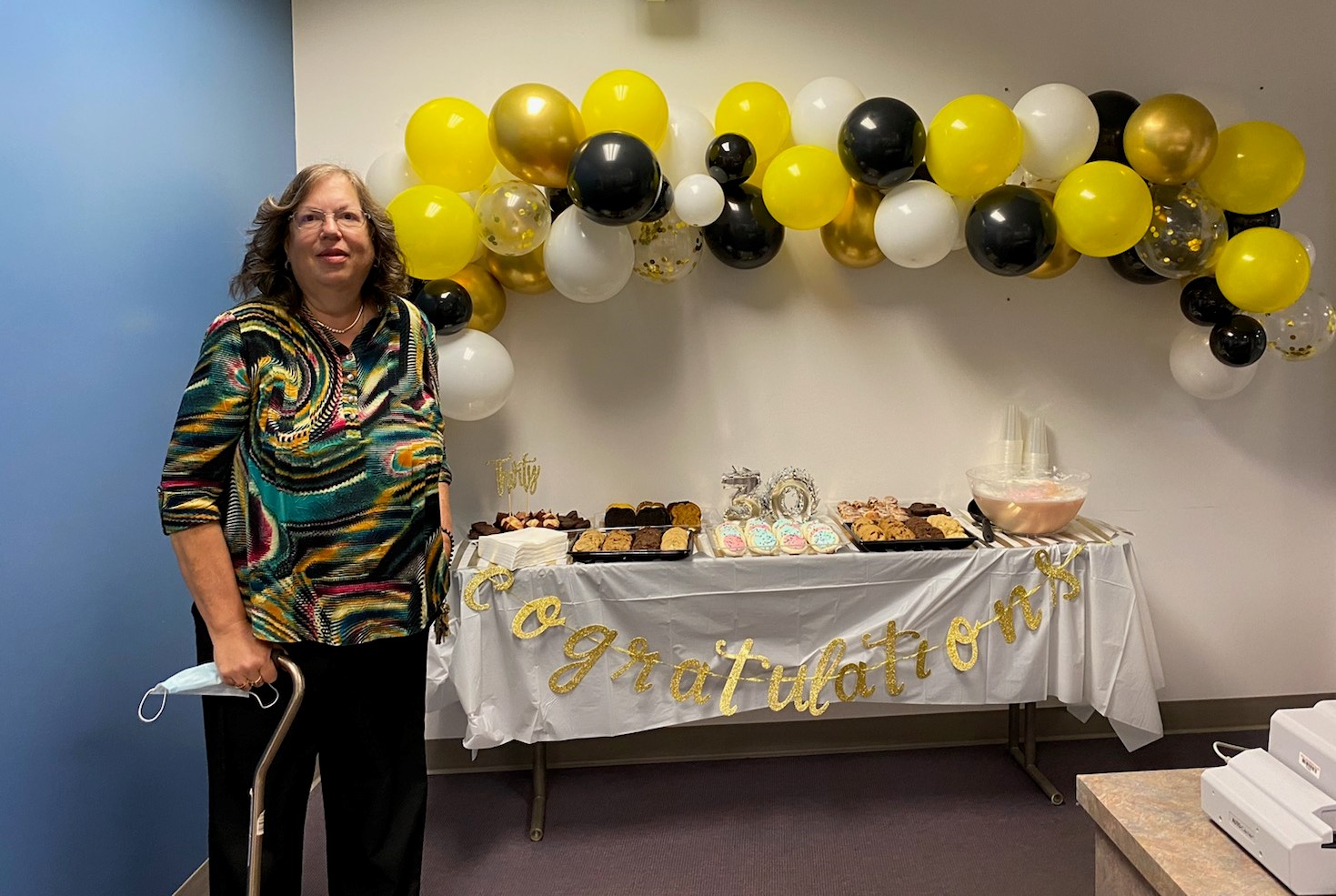 Nina Koch in front of a dessert table to celebrate her 30th Anniversary with LLCC. Banner says Congratulations.