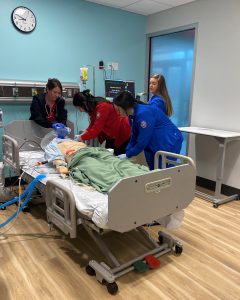 Nursing students in blue scrubs and respiratory care students in red scrubs in sim lab assisting mannequin patient