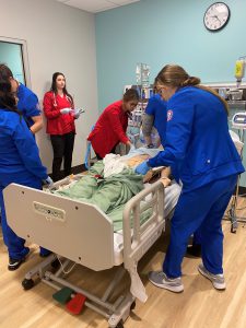 Nursing students in blue scrubs and respiratory care students in red scrubs assisting mannequin patient in sim lab