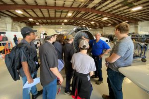 Dave Pietrzak talking to a group of students in front of a plane in the hangar
