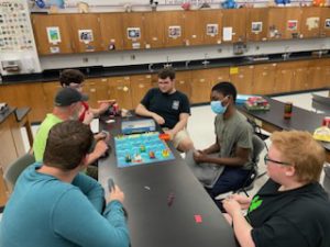 A professor and five students playing a board game.