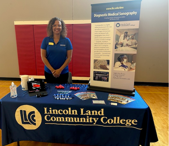 Leigh Giles-Brown at LLCC table with giveaways and display.