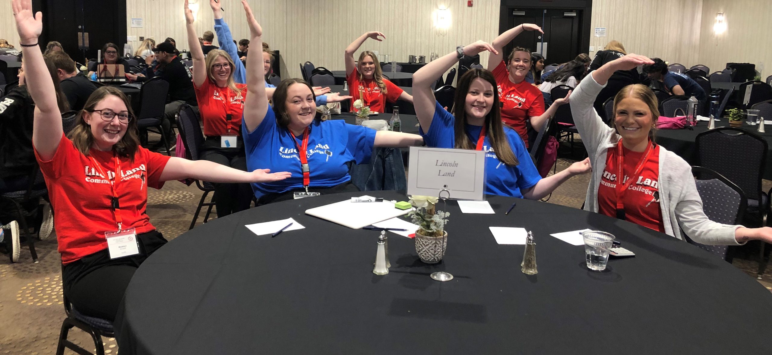 LLCC Radiography students sitting at round conference tables, spelling out LLCC with their arms.