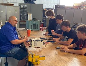 Arnold Tullis working with students at workbench in the aviation hangar