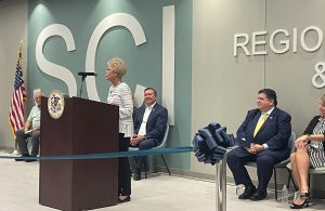 Dr. Charlotte Warren speaking at the SCI ribbon cutting. Governor Pritzker seated in background.