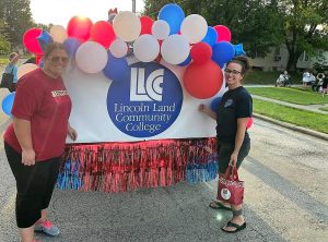 Two staff members standing by the back of the float which has balloons and the LLCC logo