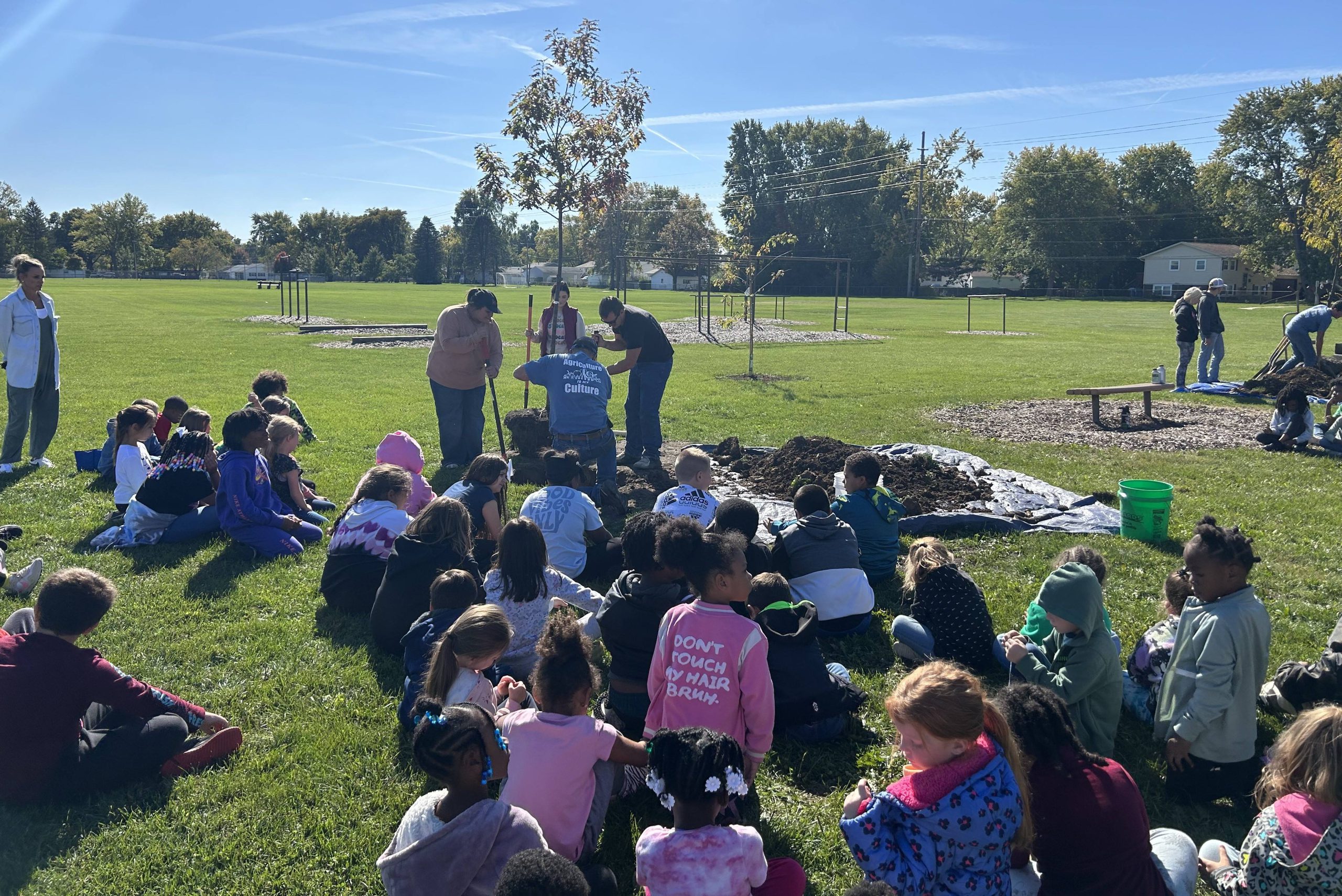 Ag Club students planting a tree with elementary students looking on