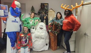 Five staff members wearing ugly holiday sweaters and posing with Linc and the abominable snowman
