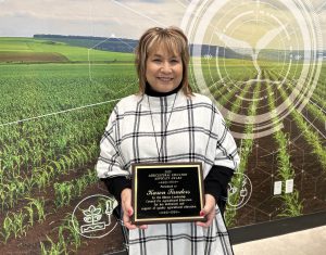 Karen Sanders holding plaque in front of wall with ag-themed graphics
