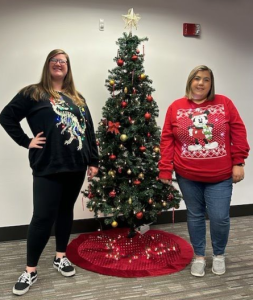 Finance staff members wearing ugly holiday sweaters standing next to tree.