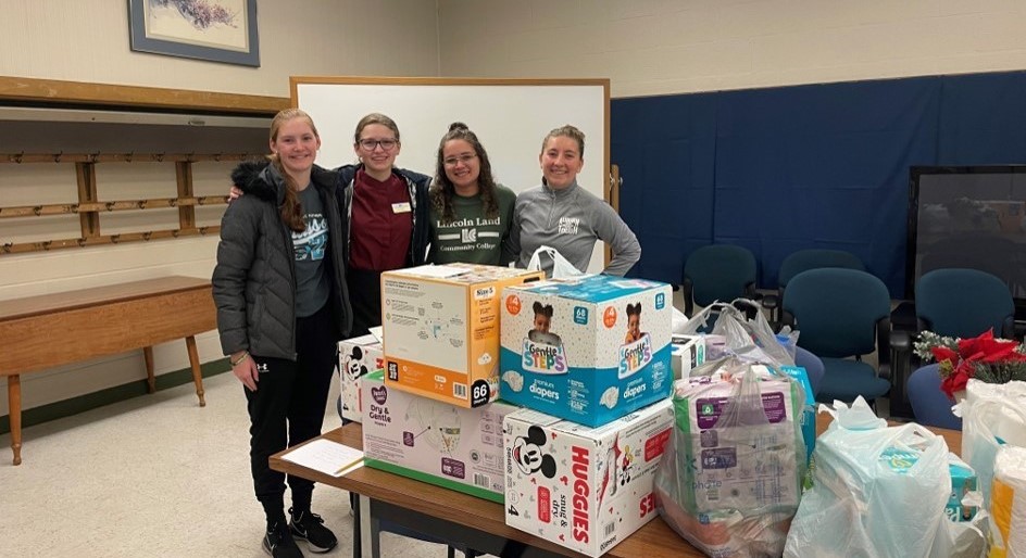 Four Honors Program students standing by a table filled with collected supplies