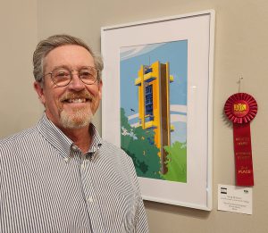 Greg Walbert standing next to his red second-place ribbon “Hear the Bells Ringing,” which is an image of a carillon behind trees made out of a variety of paper.