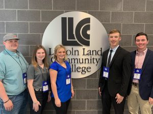 LLCC ag students posting in front of an LLCC wall logo.