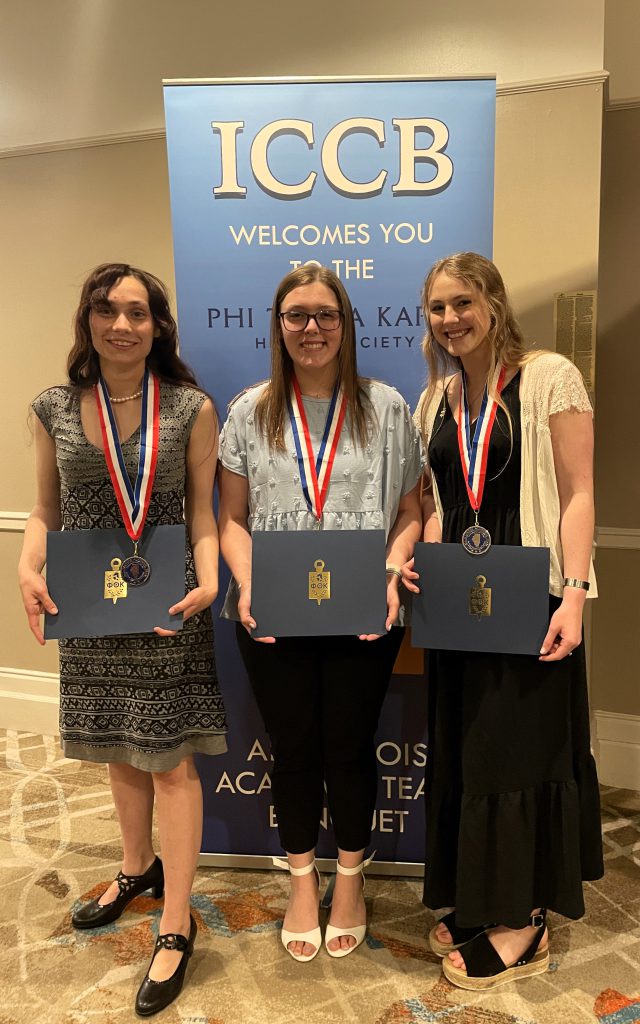 Farren Ackerman, Amelia Horn and Olivia Marchizza standing with certificates in front of ICCB banner.