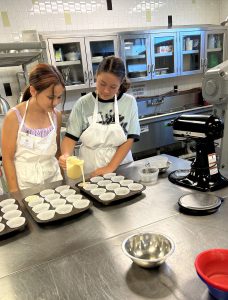 Two students pouring batter into cupcake tins