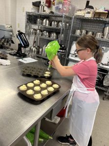 Student adding icing to the pans of cupcakes