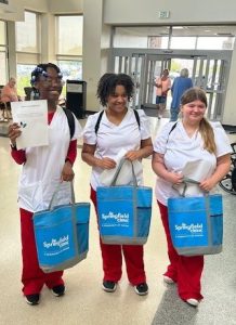 Three HELPrS participants in the lobby of a healthcare facility. Each one is holding a tote bag with the words Springfield Clinic on it. This was a gift given to them by the 2024 HELPrS program sponsor.