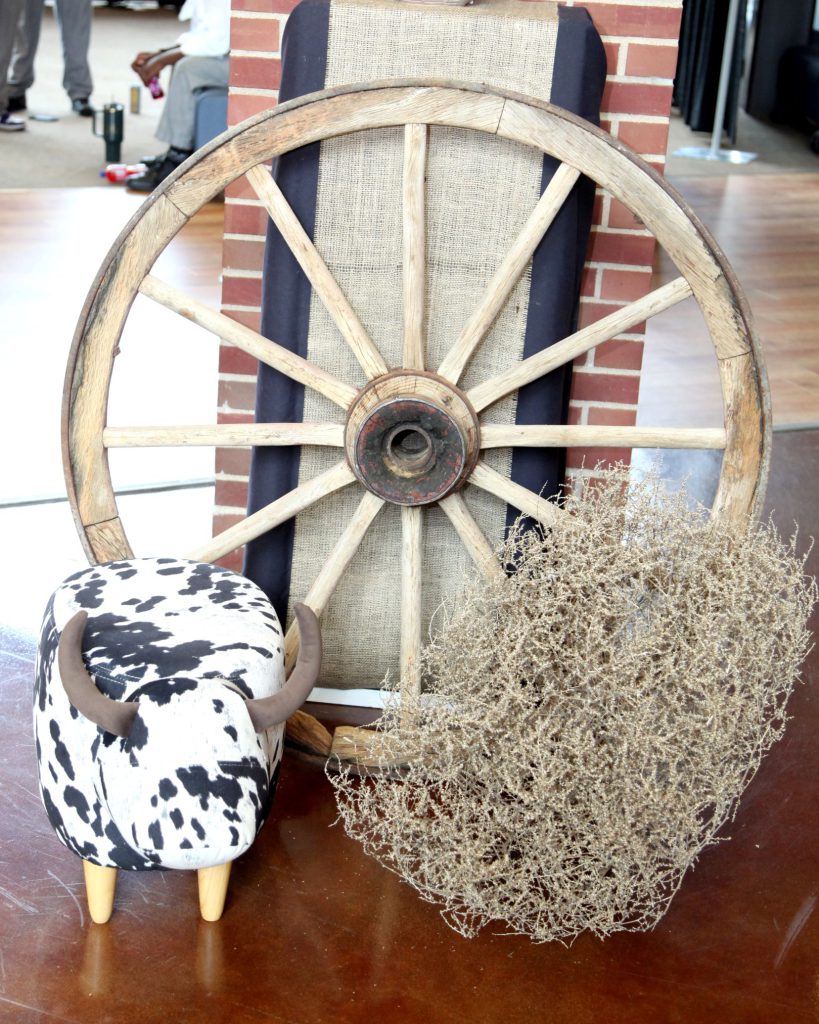 A decorative tumbleweed against a wagon wheel and decorative cow.