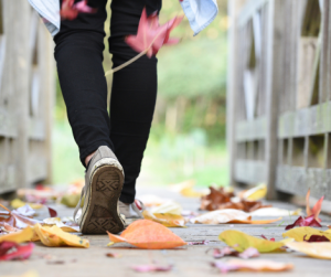 A person's feet walking in the fall leaves.