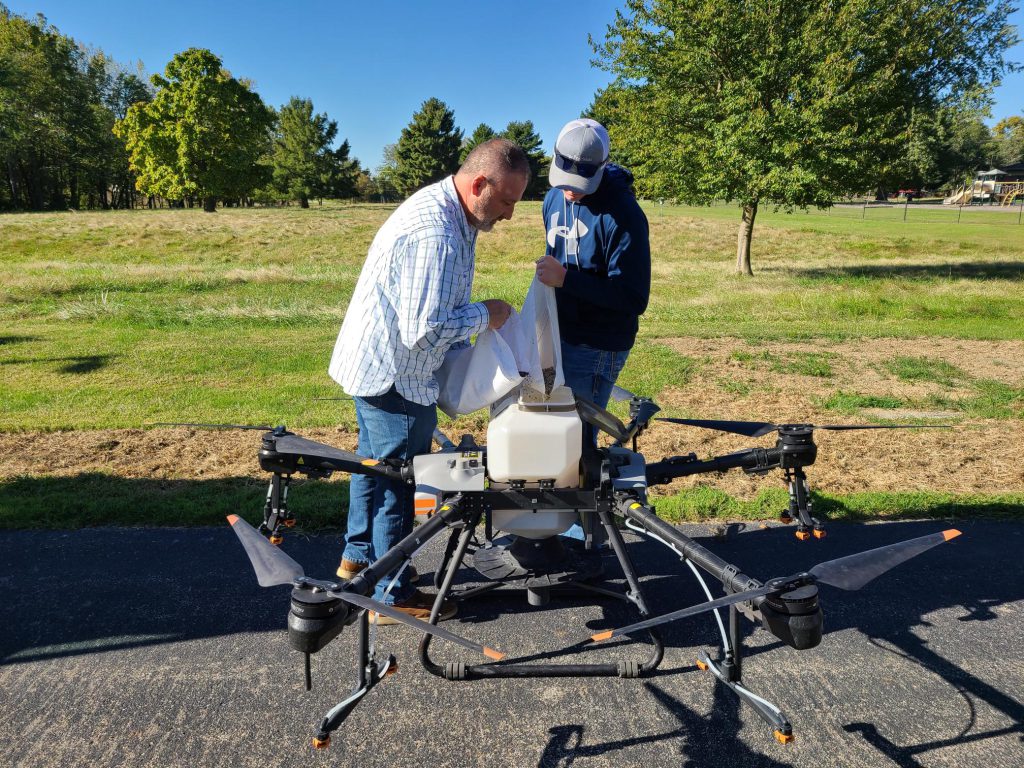 LLCC instructor pouring seed into a large agriculture drone.