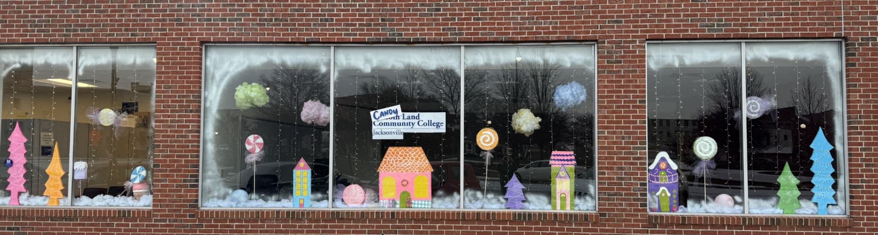 Three windows decorated with houses, pine trees and lollipops amid snow painted on the windows.