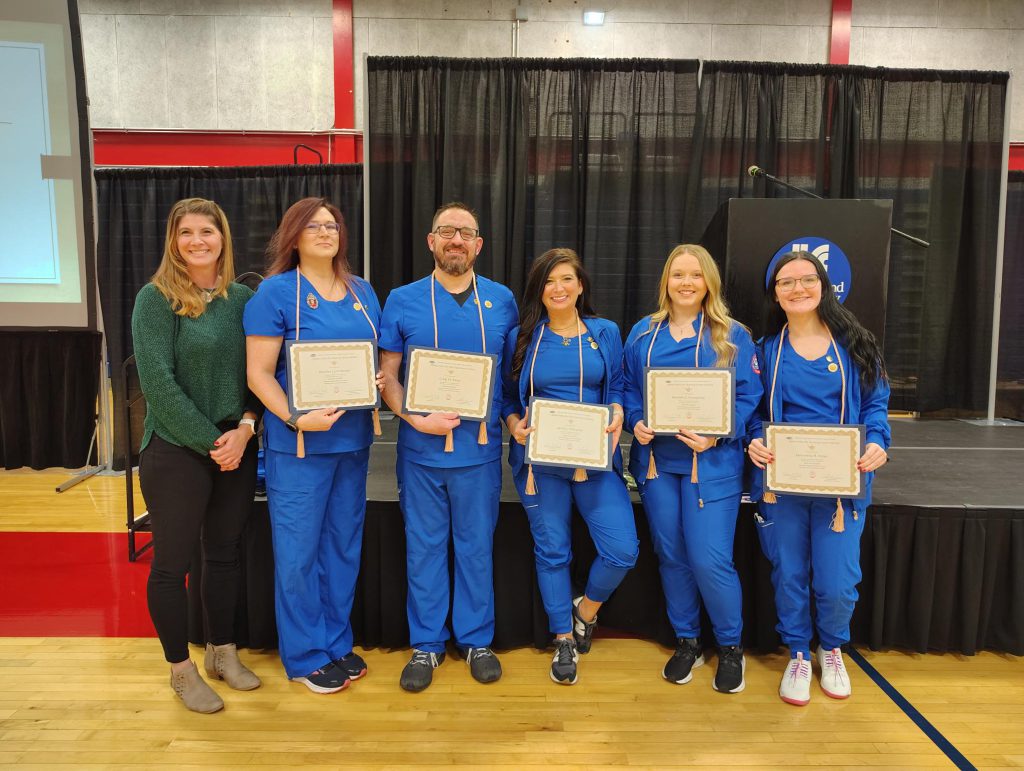 Five nurses in blue scubs holding certificates for Alpha Delta Nu.