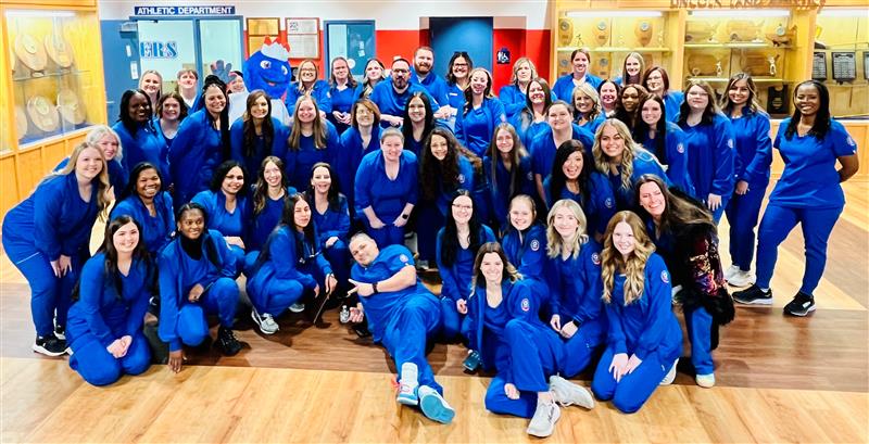 Large group of nursing students in blue scrubs posing for a photo.